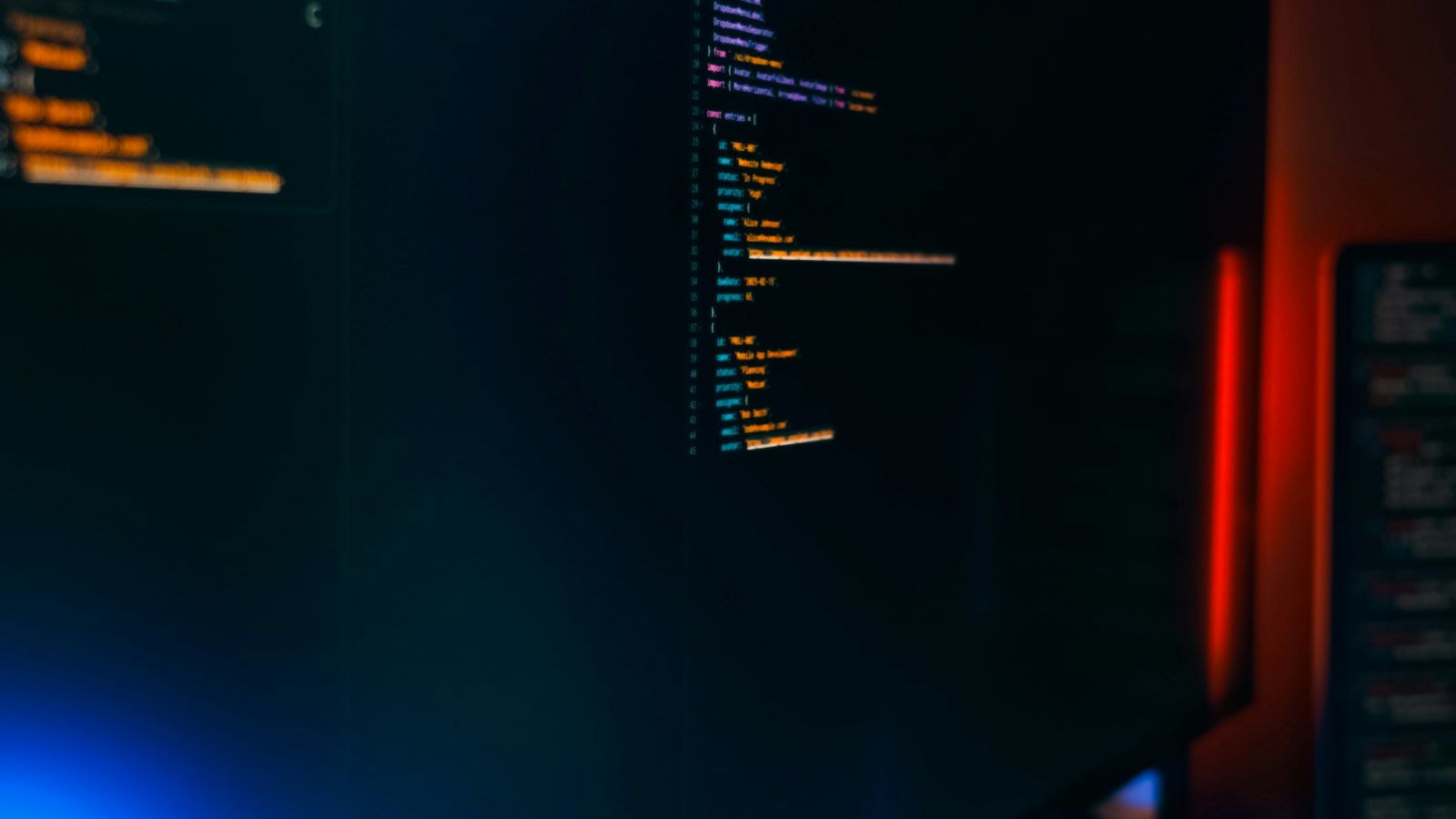A dark screen glowing with lines of code, lit by ambient red and blue light
